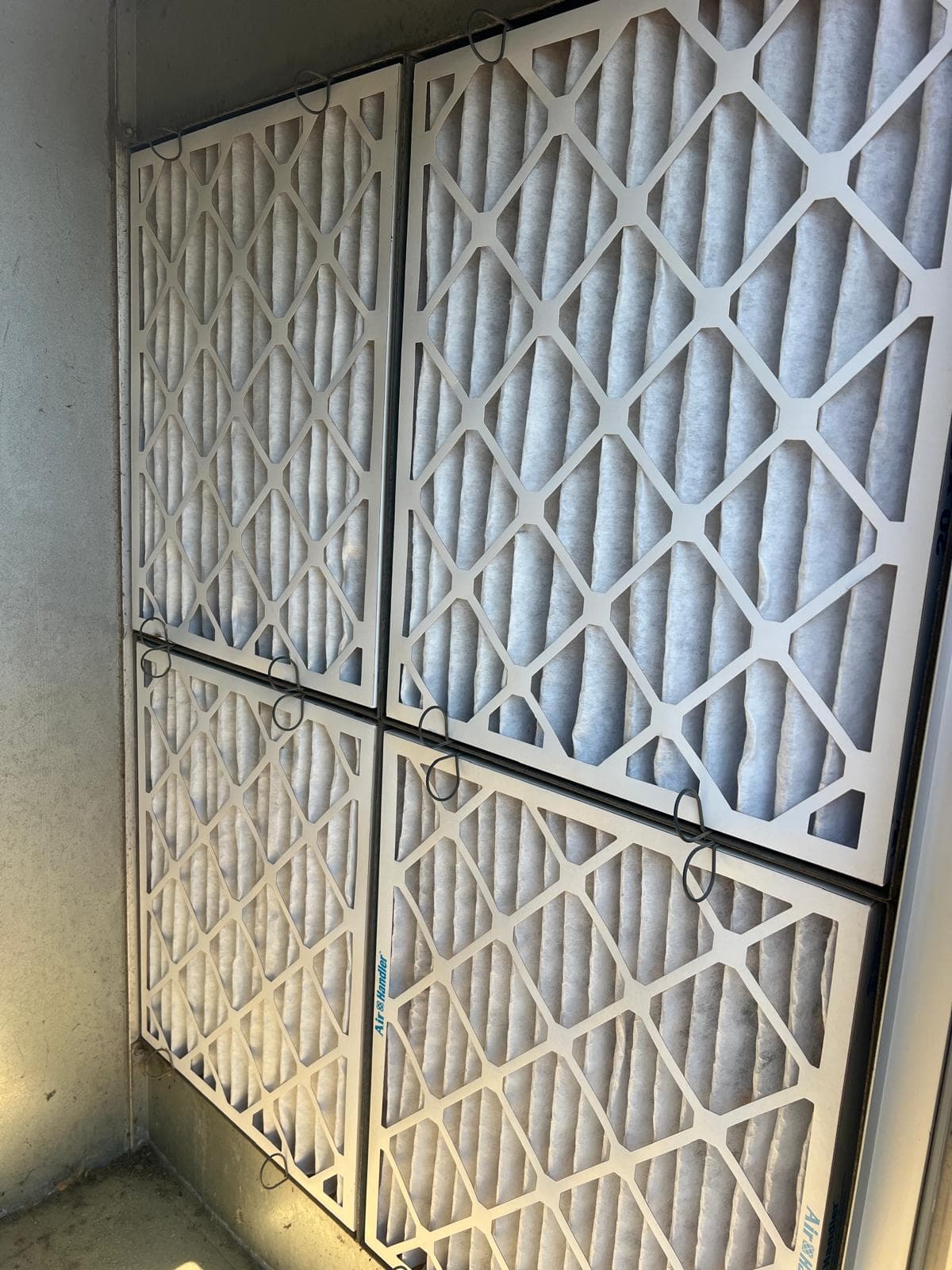 A four-panel return-air filter bank clogged dark brown with dust before service, replaced with clean white pleated filters afterwards